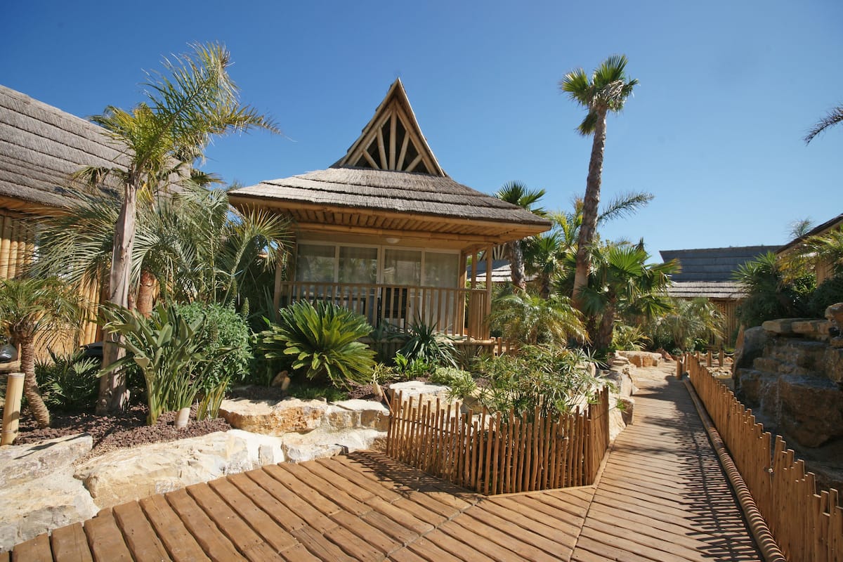 A resort with a thatched-roof building, wooden deck, and tropical landscaping.