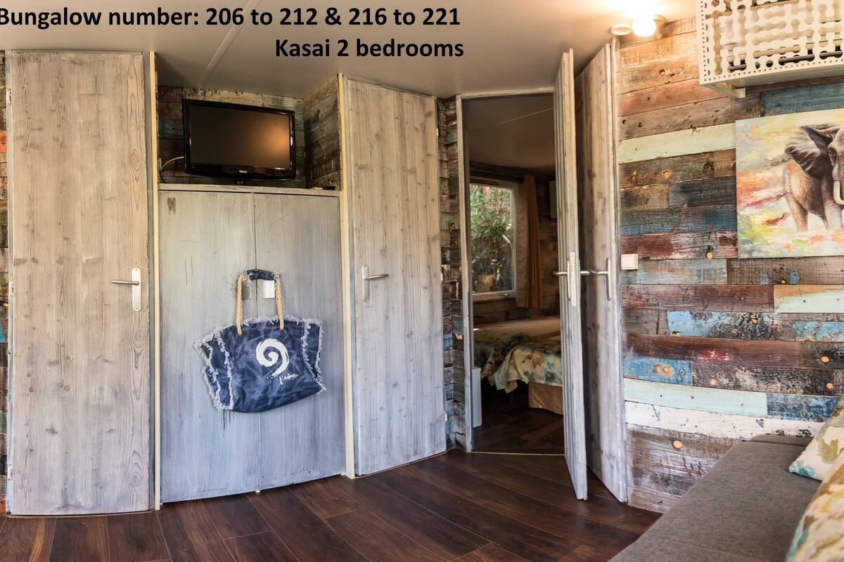 A room with a wooden wardrobe, a television, a painting of an elephant, and a sofa with floral cushions.