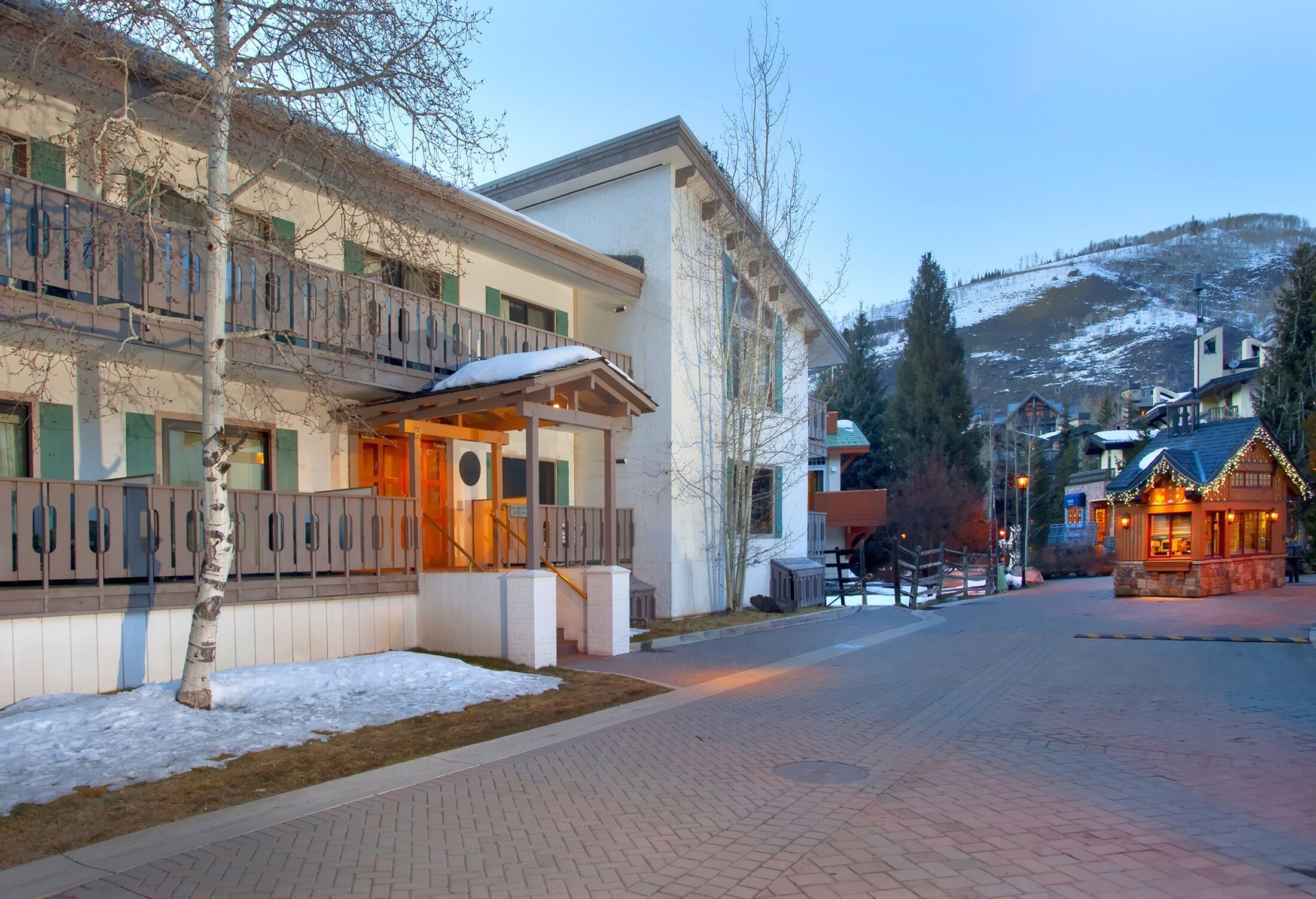 A hotel with a balcony, a snow-covered ground, and a mountain in the background.