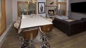 A modern dining area with a large table, bar stools, and a fireplace. - Riva Ridge 630 4 Bedroom Condo by RedAwning (Vail)