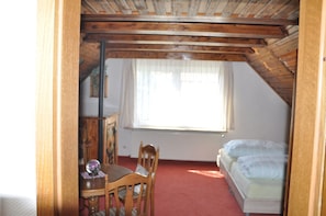 A room with a sloped ceiling, a wooden table with chairs, a bed, and a window with sheer curtains. - Pension Britzkow (Erfurt)