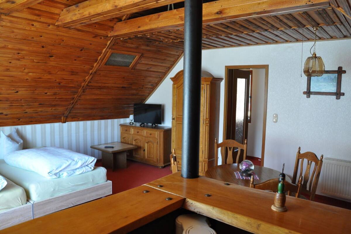A cozy attic bedroom with a wooden ceiling, a bed, a TV, a dining table, and a chair.