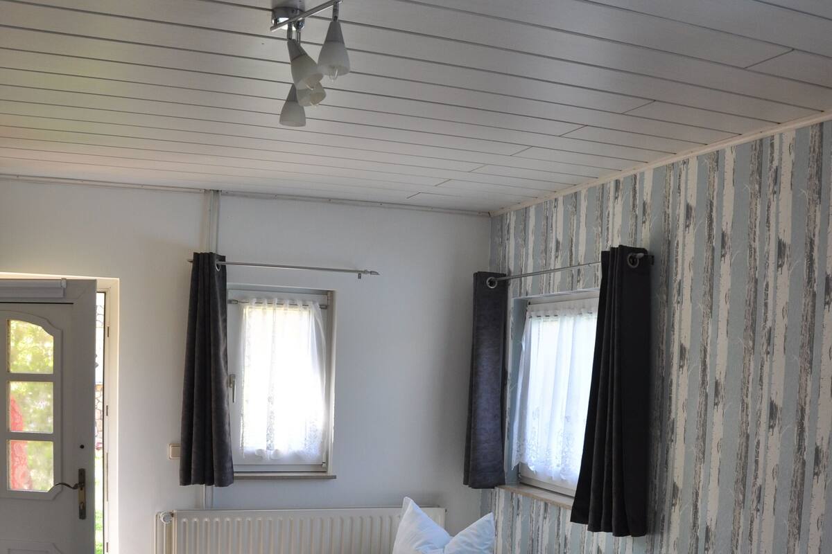 A room with a bed, a table with a menu, a radiator, and a window with curtains.