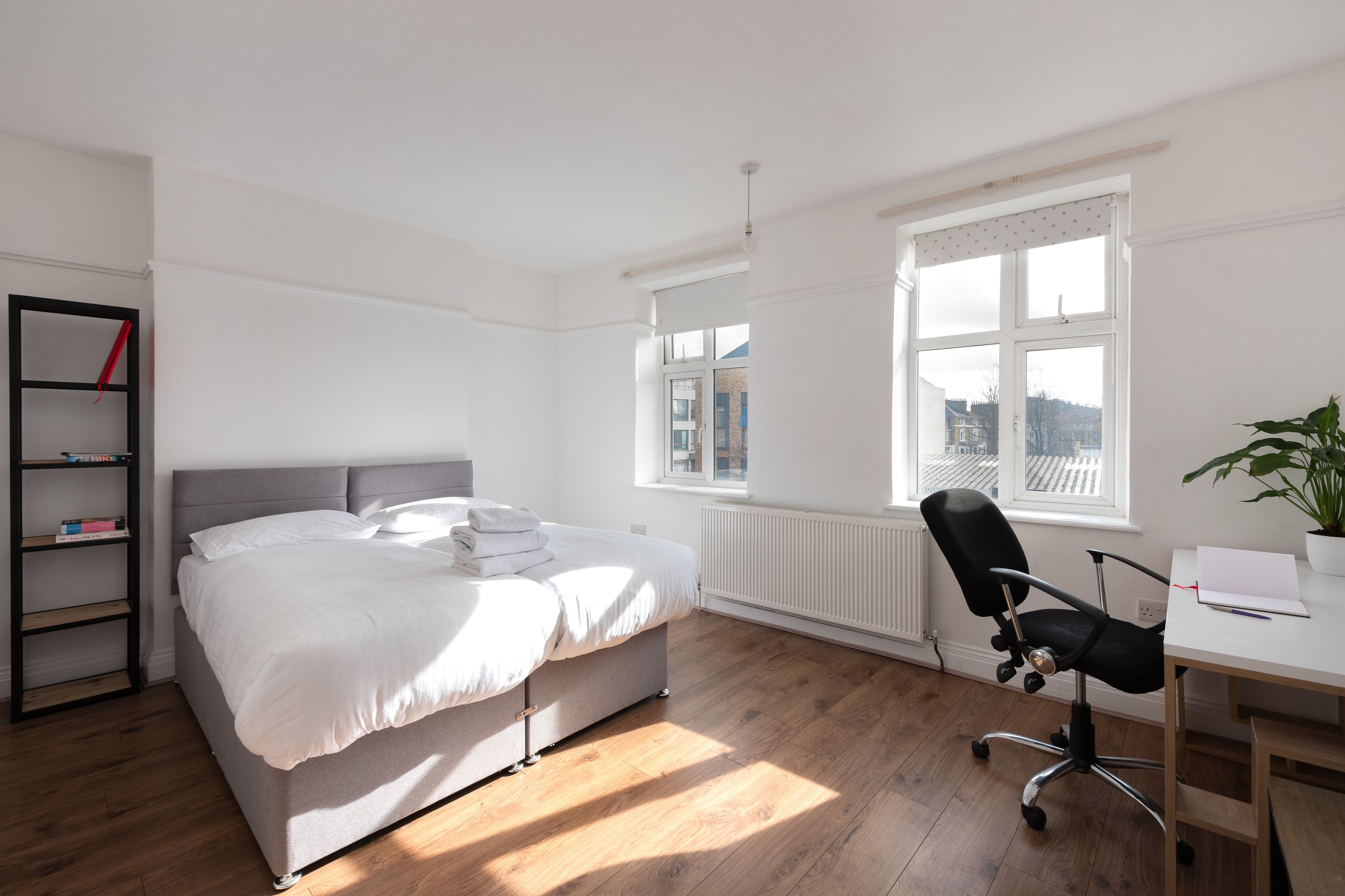 Une chambre à coucher comprenant un lit, un bureau, une chaise, un radiateur et une fenêtre donnant sur un paysage agréable.