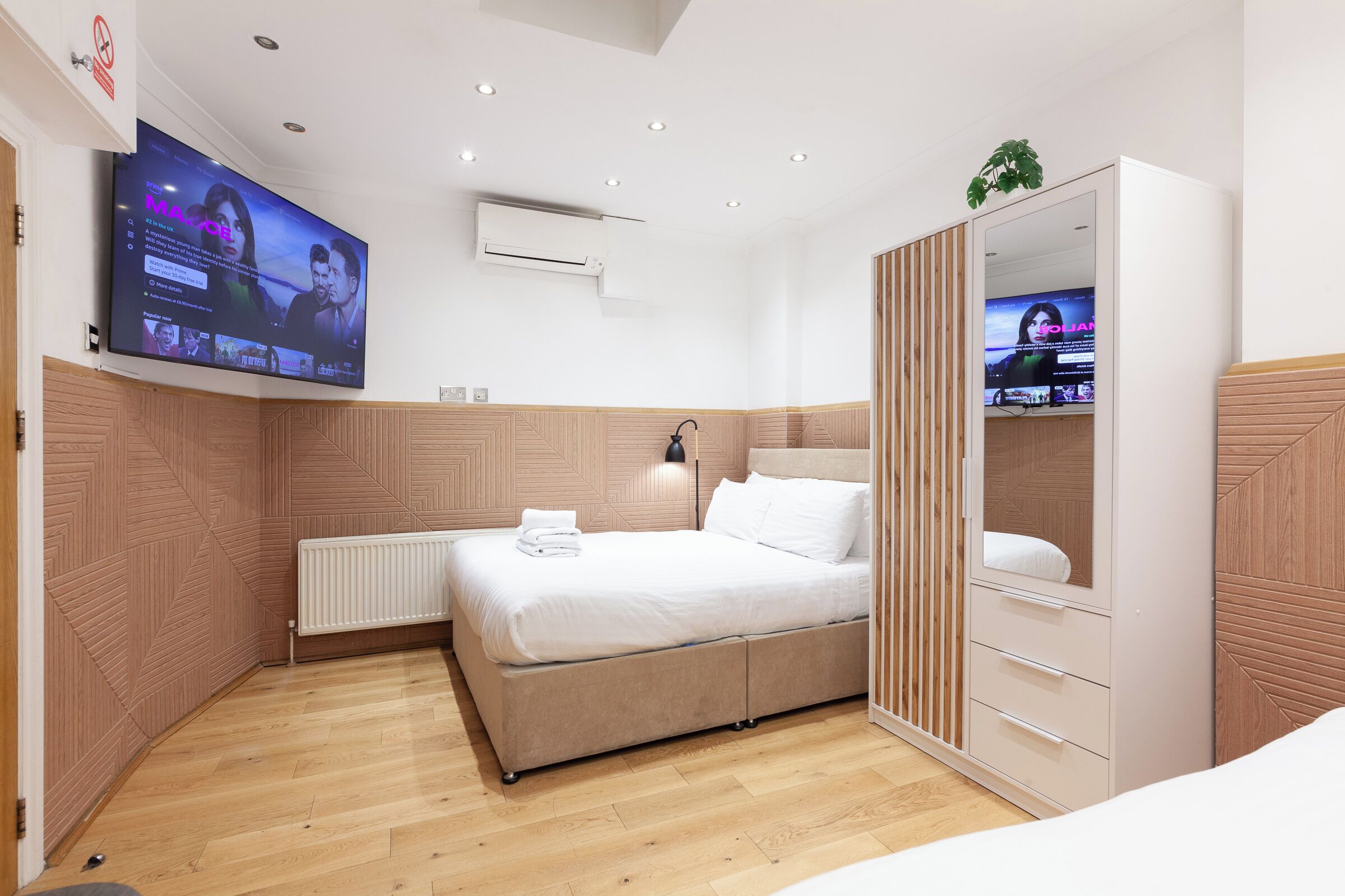 Un dormitorio moderno con una cama grande, un armario, un televisor montado en la pared y una lámpara en el techo.