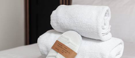 A neatly made bed with white towels and slippers, a wooden headboard, and a white pillow.