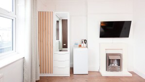 A modern living room with a fireplace, a flat-screen TV mounted on the wall, and a sliding door with striped curtains. - Argyle Apart Hotel (London)