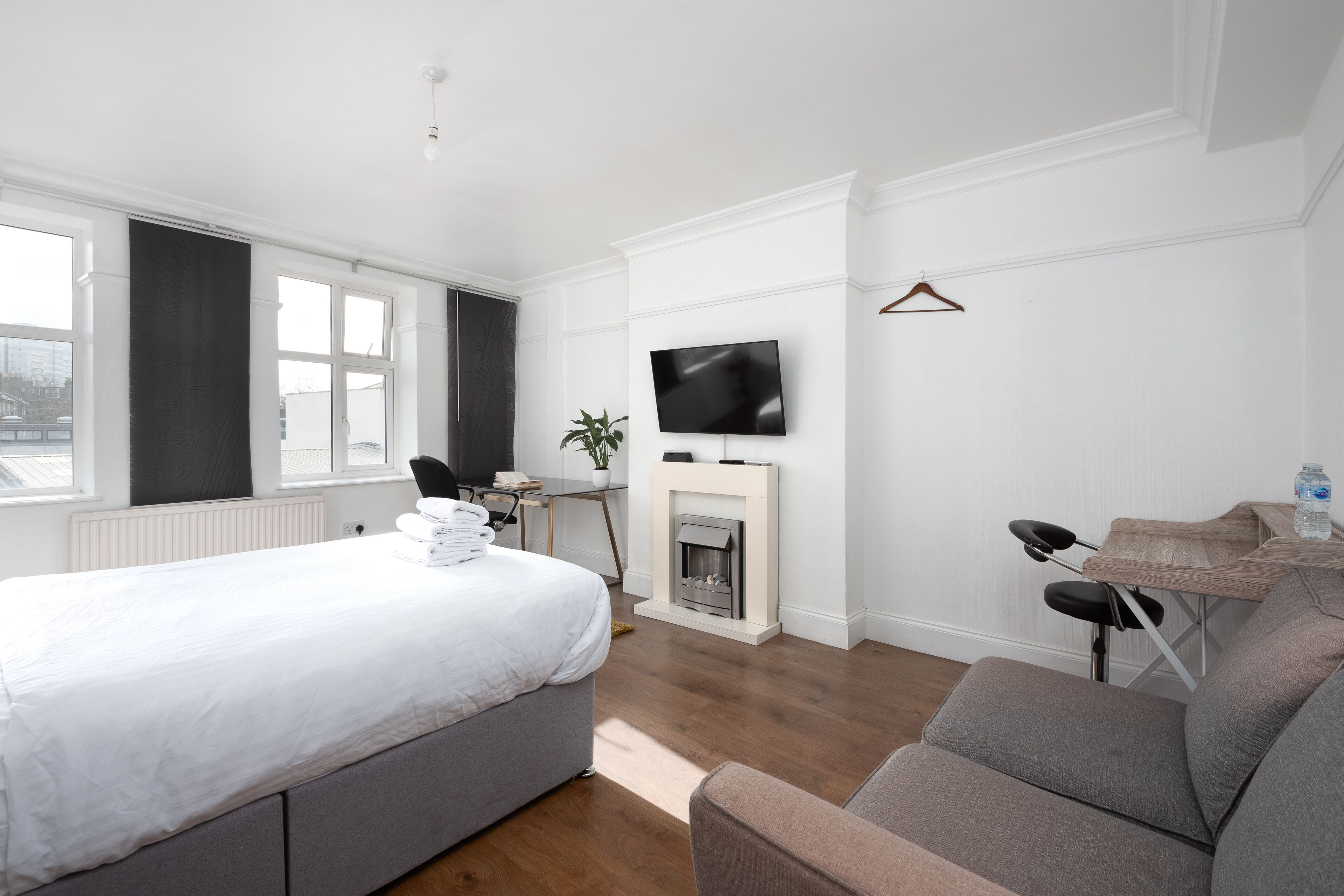 Ein modernes Hotelzimmer mit einem großen Bett, einem grauen Sofa, einem an der Wand befestigten Fernseher und einem Kamin.