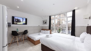 A hotel room with a bed, a desk with two chairs, a television, and a window with a view of buildings. - Argyle Apart Hotel (London)