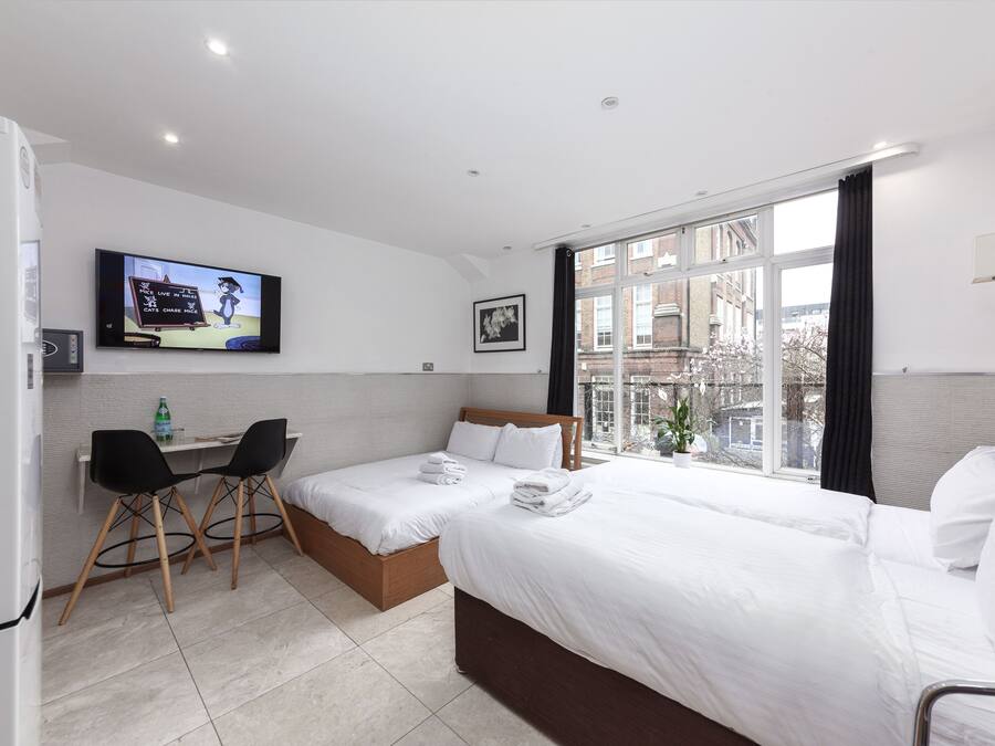 Habitación de hotel con cama, escritorio con dos sillas, televisión y ventana con vista a edificios.
