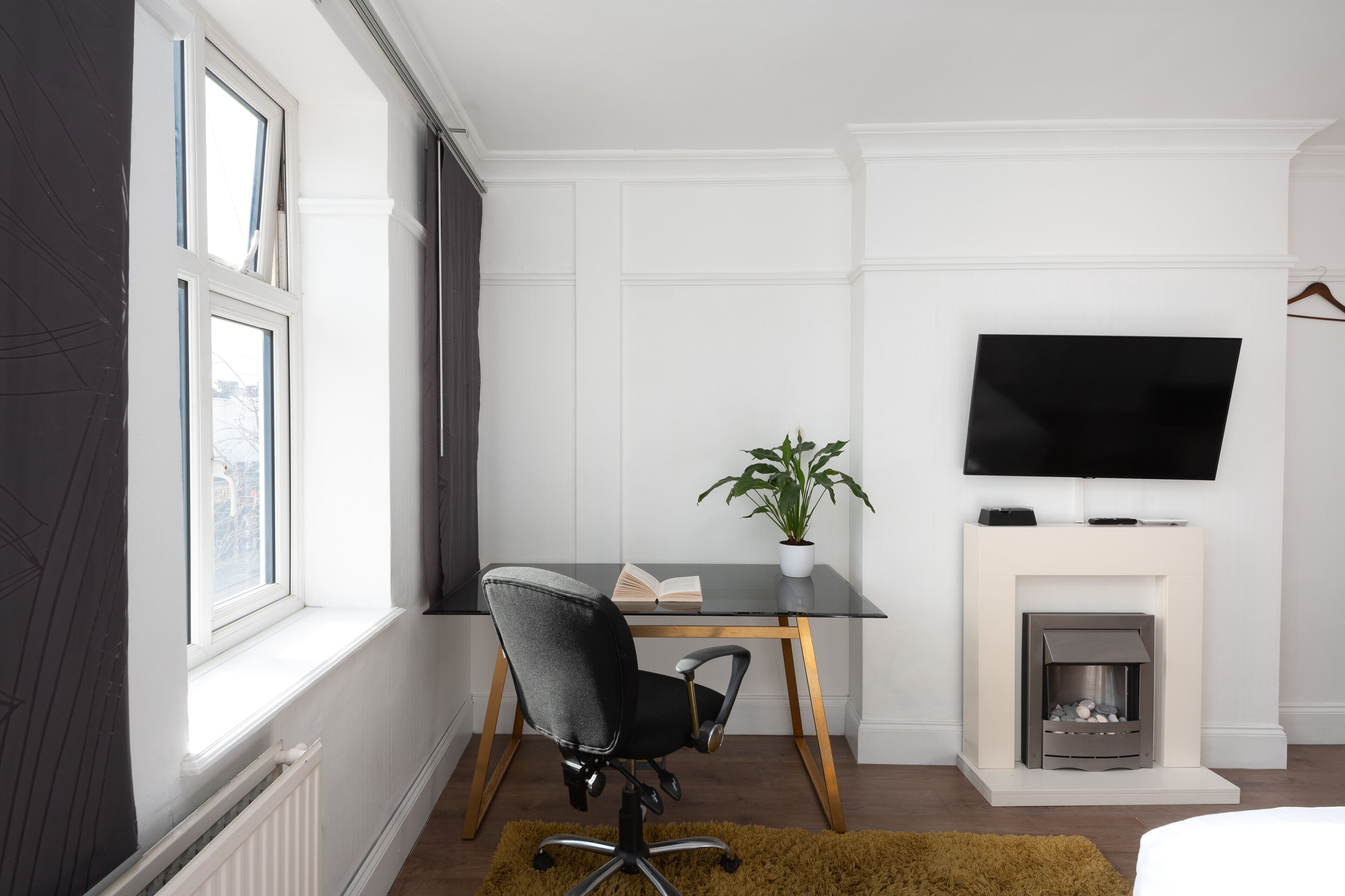 A modern hotel room with a desk, chair, TV, fireplace, and a window with curtains.