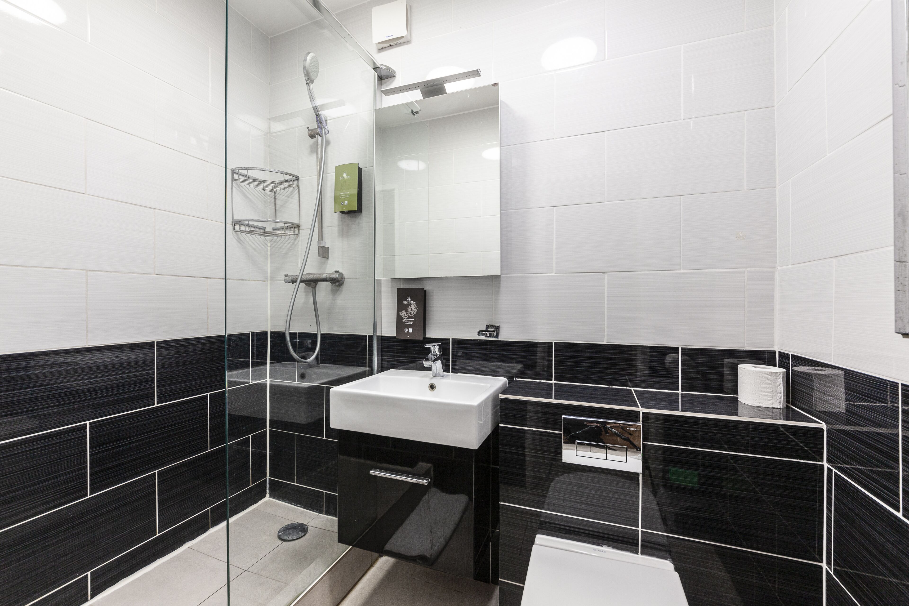 A modern bathroom with a glass-enclosed shower, a white sink, and black-tiled walls.