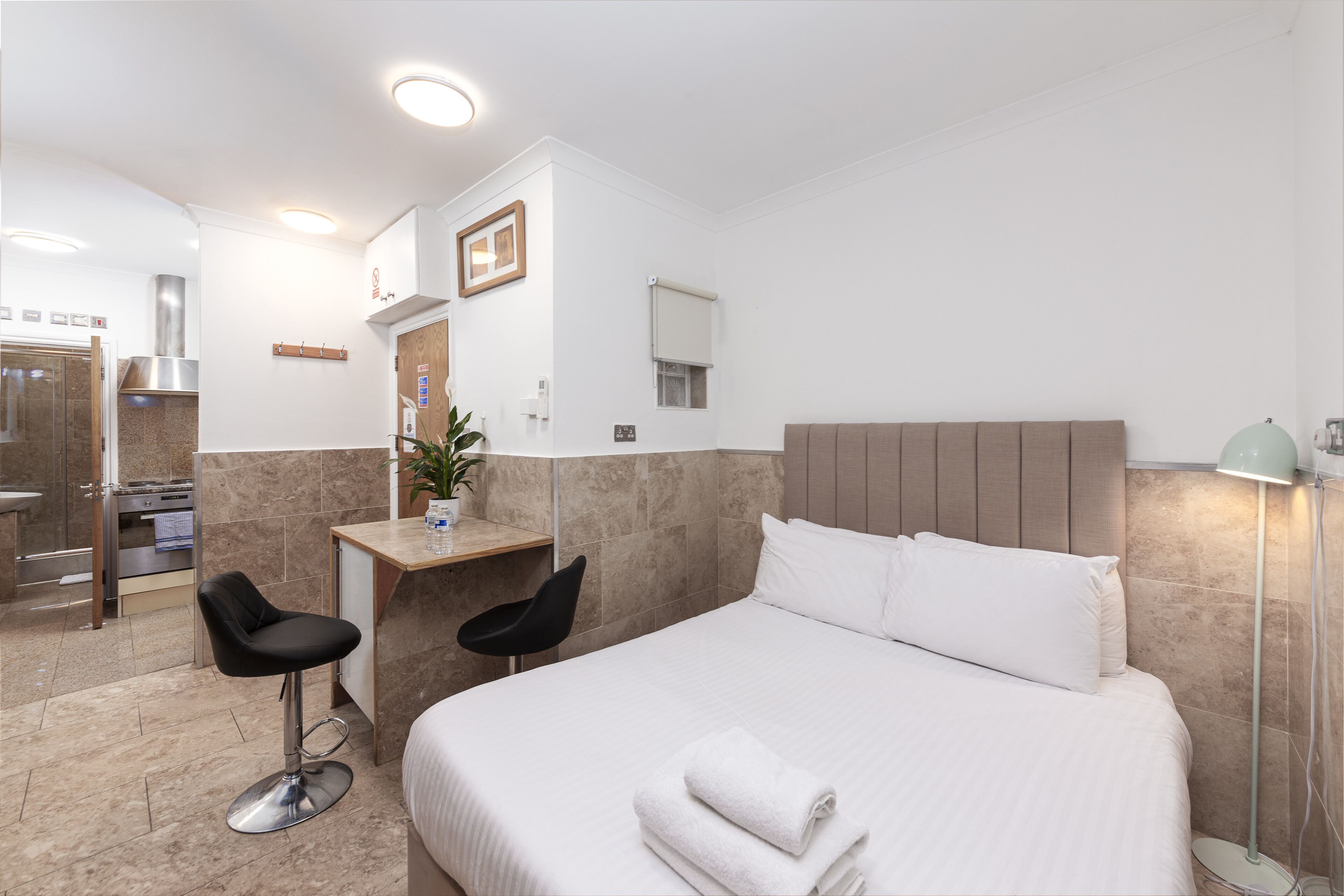 Habitación de hotel con cama, dos sillas, un escritorio, un espejo y baño visible a través de una puerta abierta.
