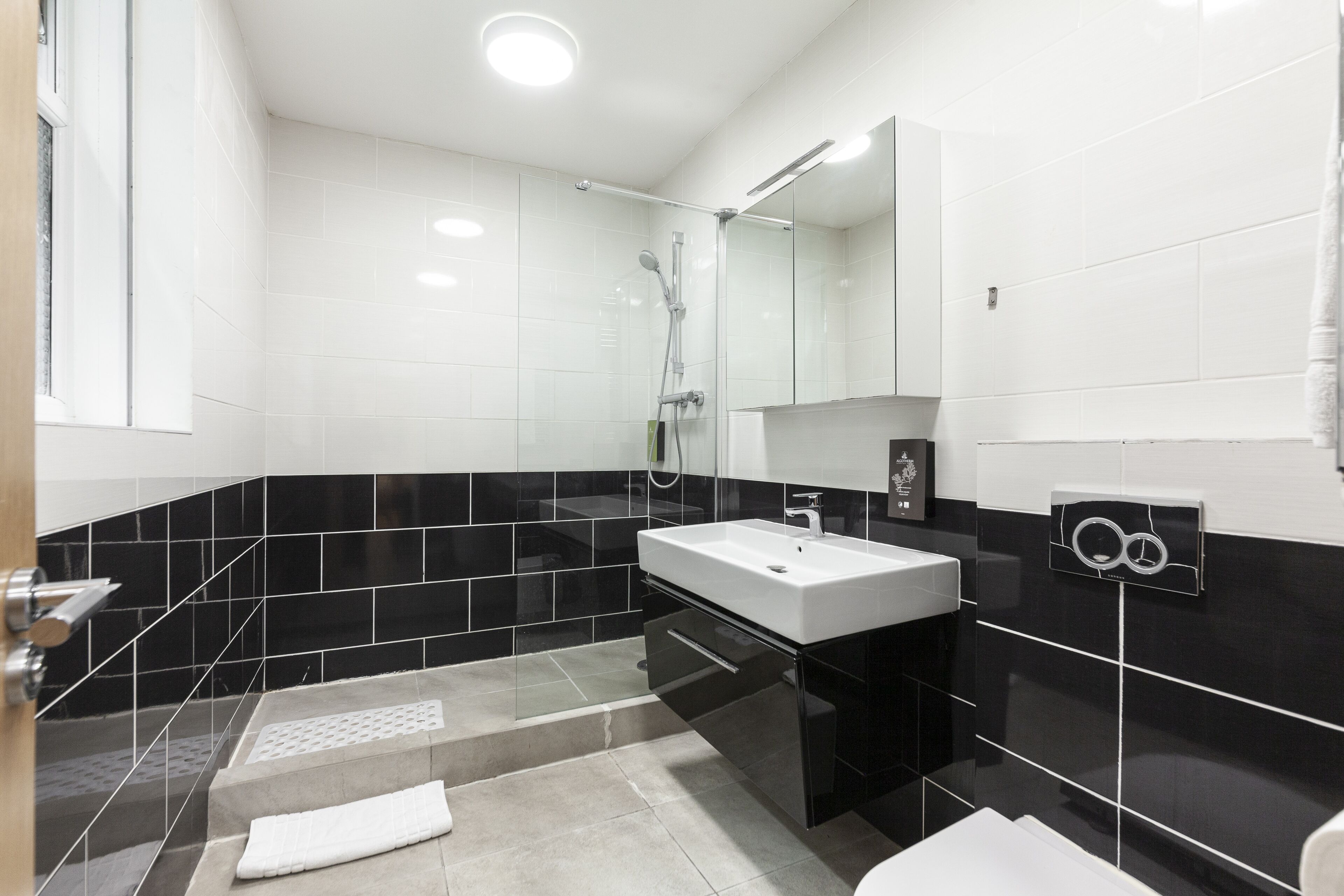 Une salle de bain moderne avec un lavabo blanc, des carreaux noirs et blancs, une cabine de douche en verre et un miroir au-dessus du lavabo.