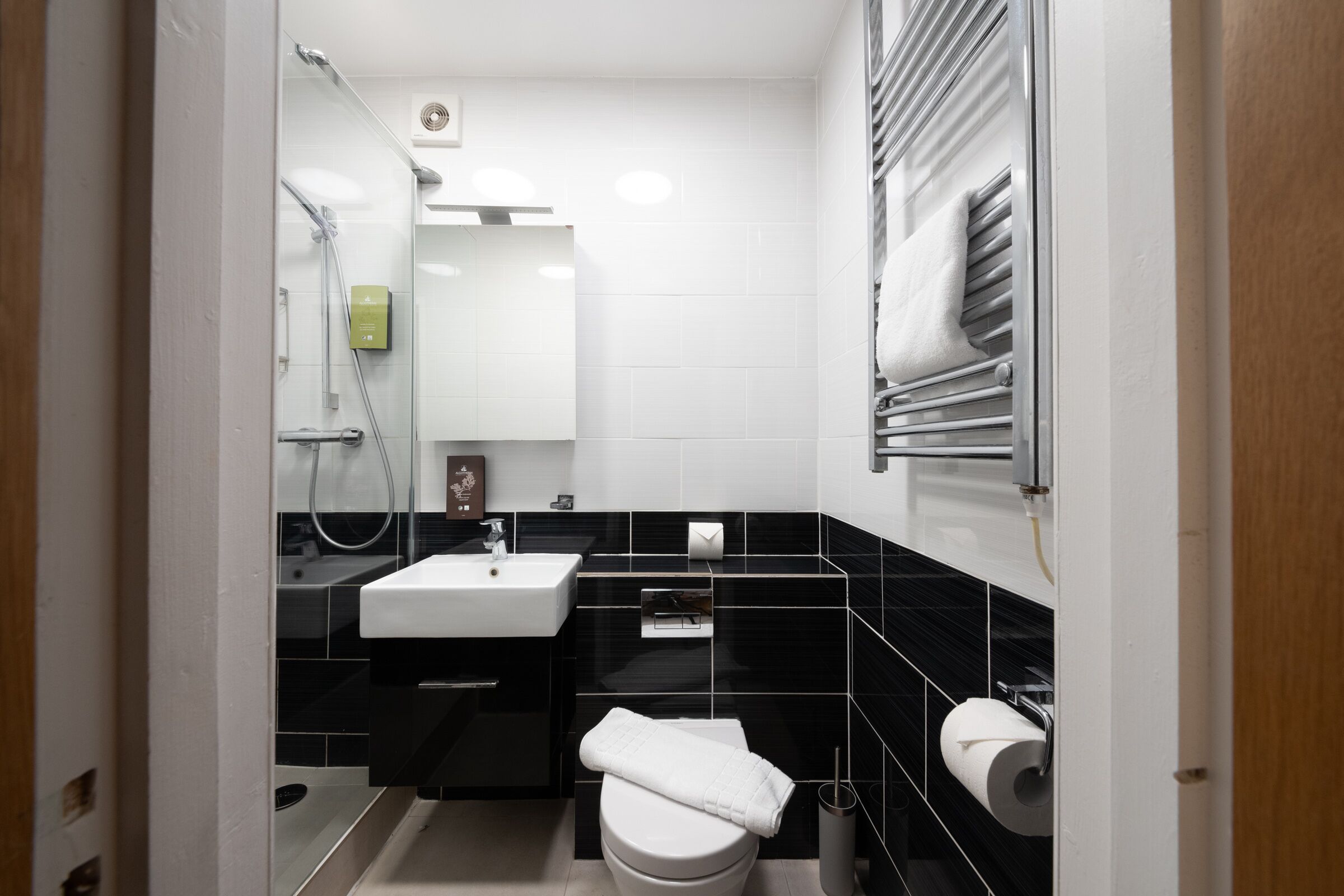 A modern bathroom with a white sink, black tiled walls, a toilet, and a towel rack.