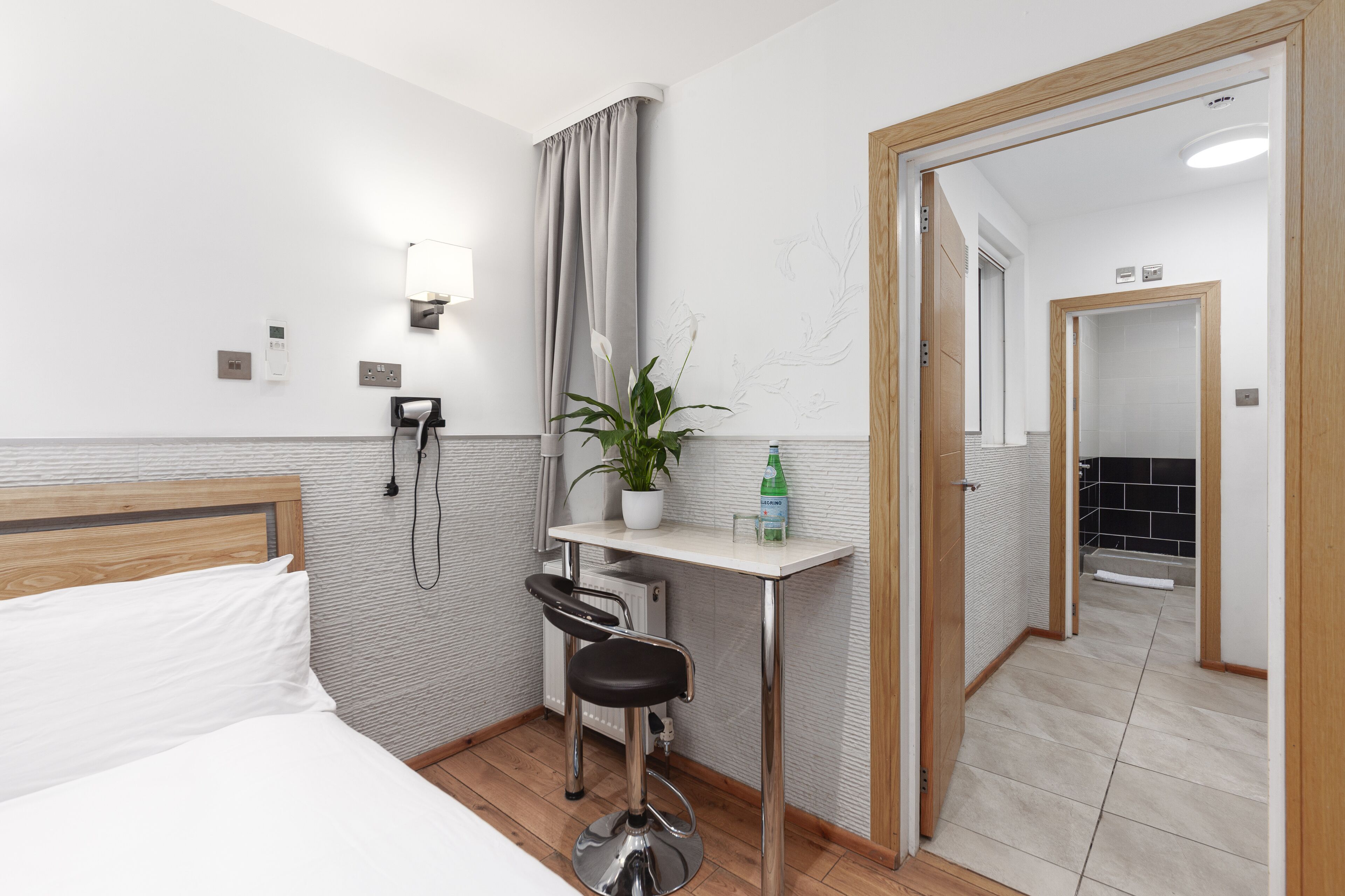 Habitación de hotel con cama, escritorio con silla, planta, dispensador de gel antibacterial y espejo.