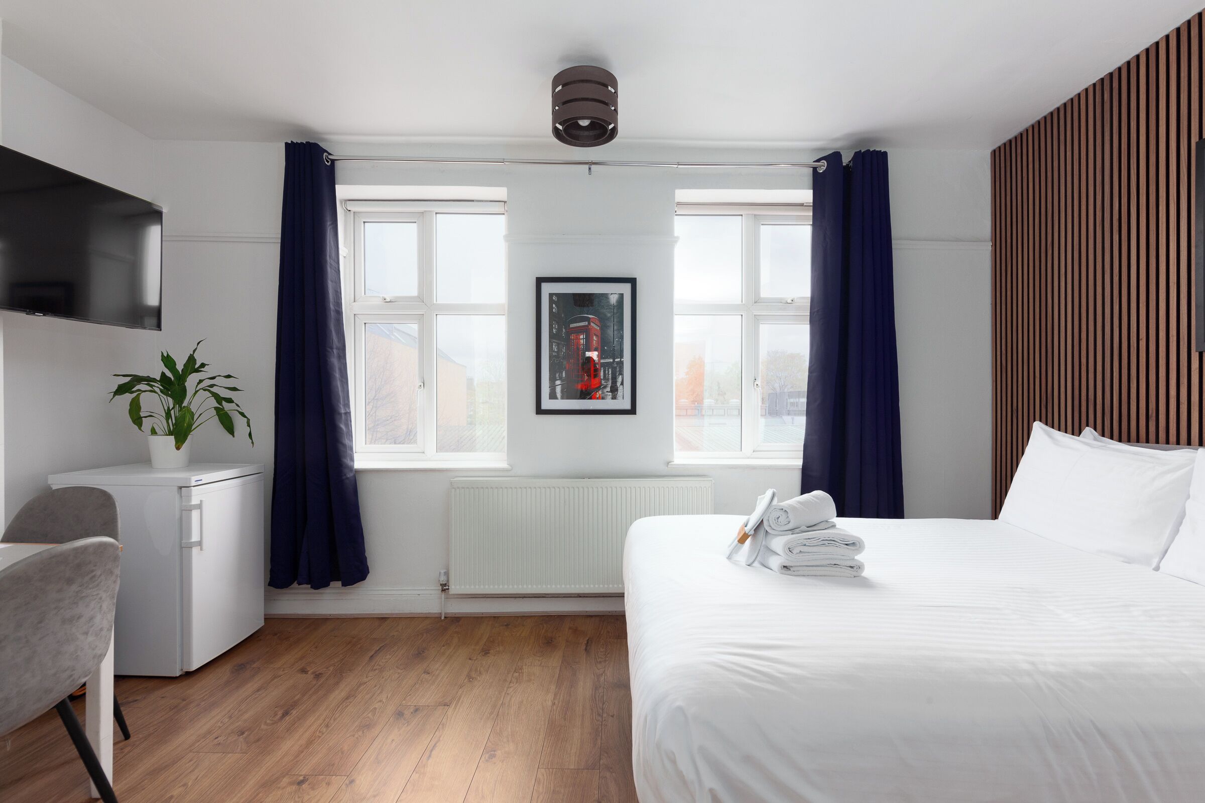 A hotel room with a bed, a desk, a chair, a radiator, and a window with curtains.