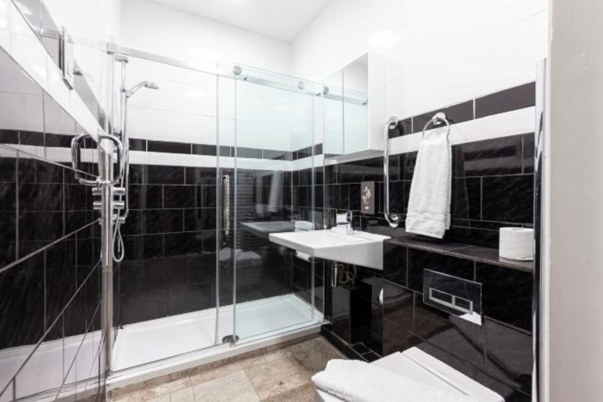 A modern bathroom with a glass-enclosed shower, a white sink, and a black-tiled vanity.