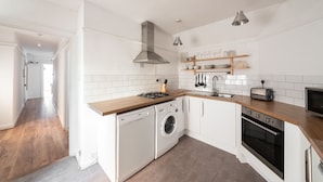 A modern kitchen with white cabinetry, a built-in washer and dryer, a stove, and a microwave. - Argyle Apart Hotel (London)