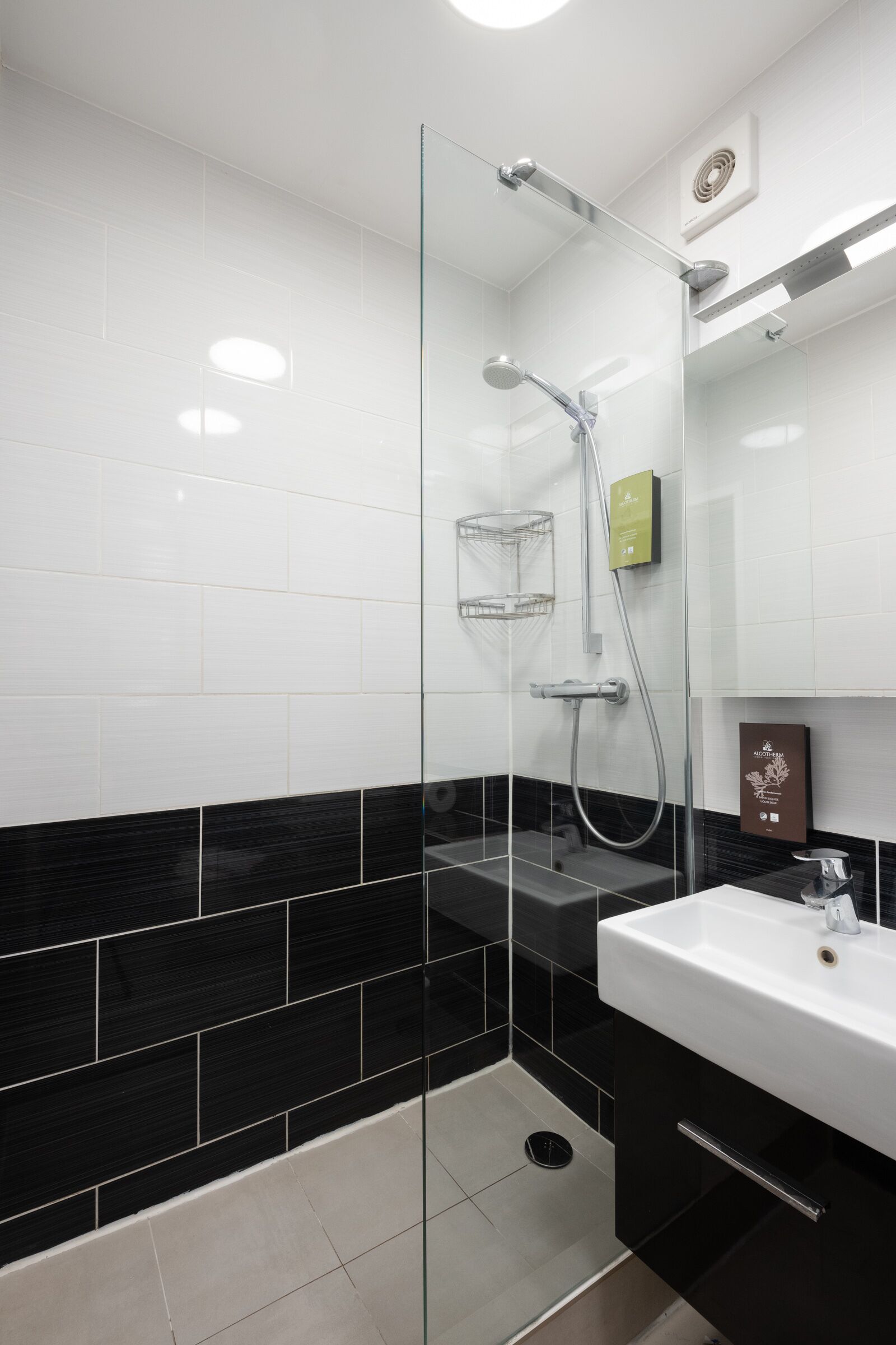 A modern bathroom with a glass-enclosed shower, a white sink, and black tiled walls.
