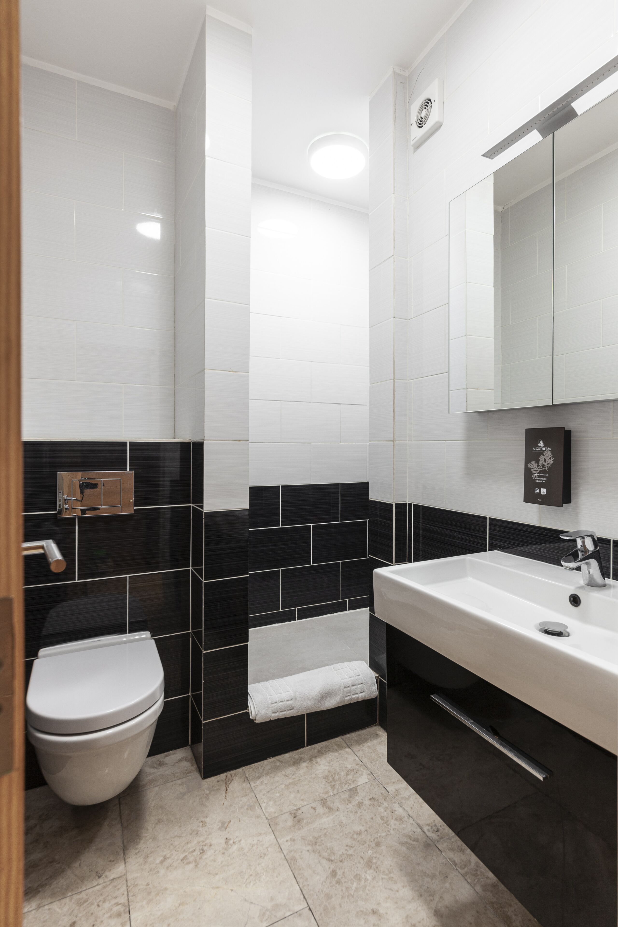 A modern bathroom with a white toilet, black and white tiled walls, a white sink, and a mirror above the sink.