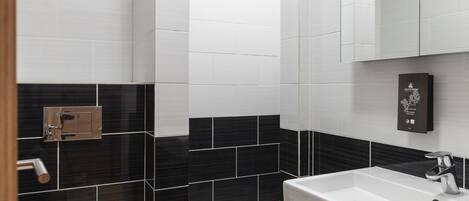 A modern bathroom with a white toilet, black and white tiled walls, a white sink, and a mirror above the sink.