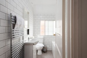 Ein modernes Badezimmer mit weißen Fliesen, einer Toilette, einem Waschbecken und einem Handtuchhalter.