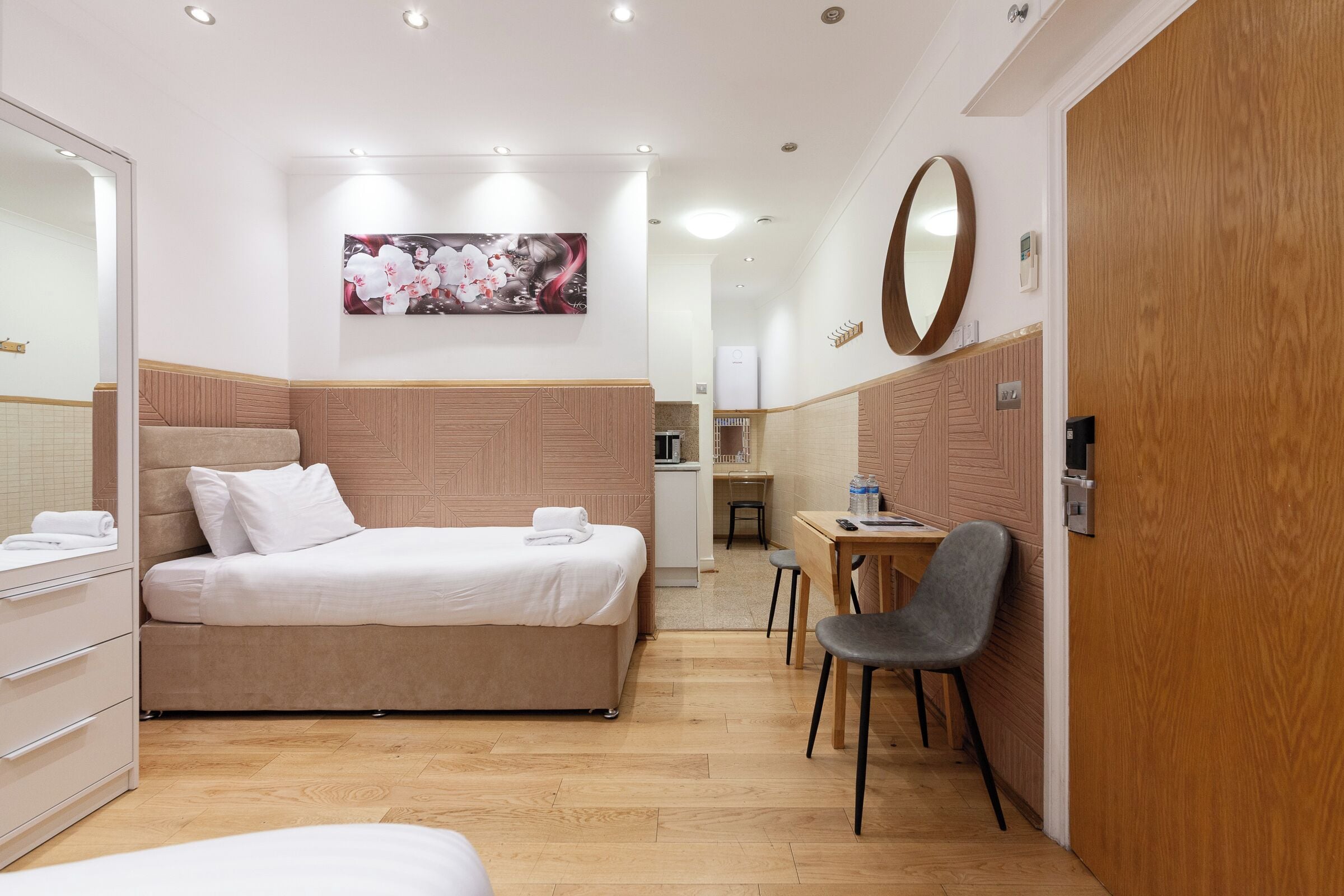 A hotel room with a bed, a desk, a chair, a wardrobe, and a mirror.