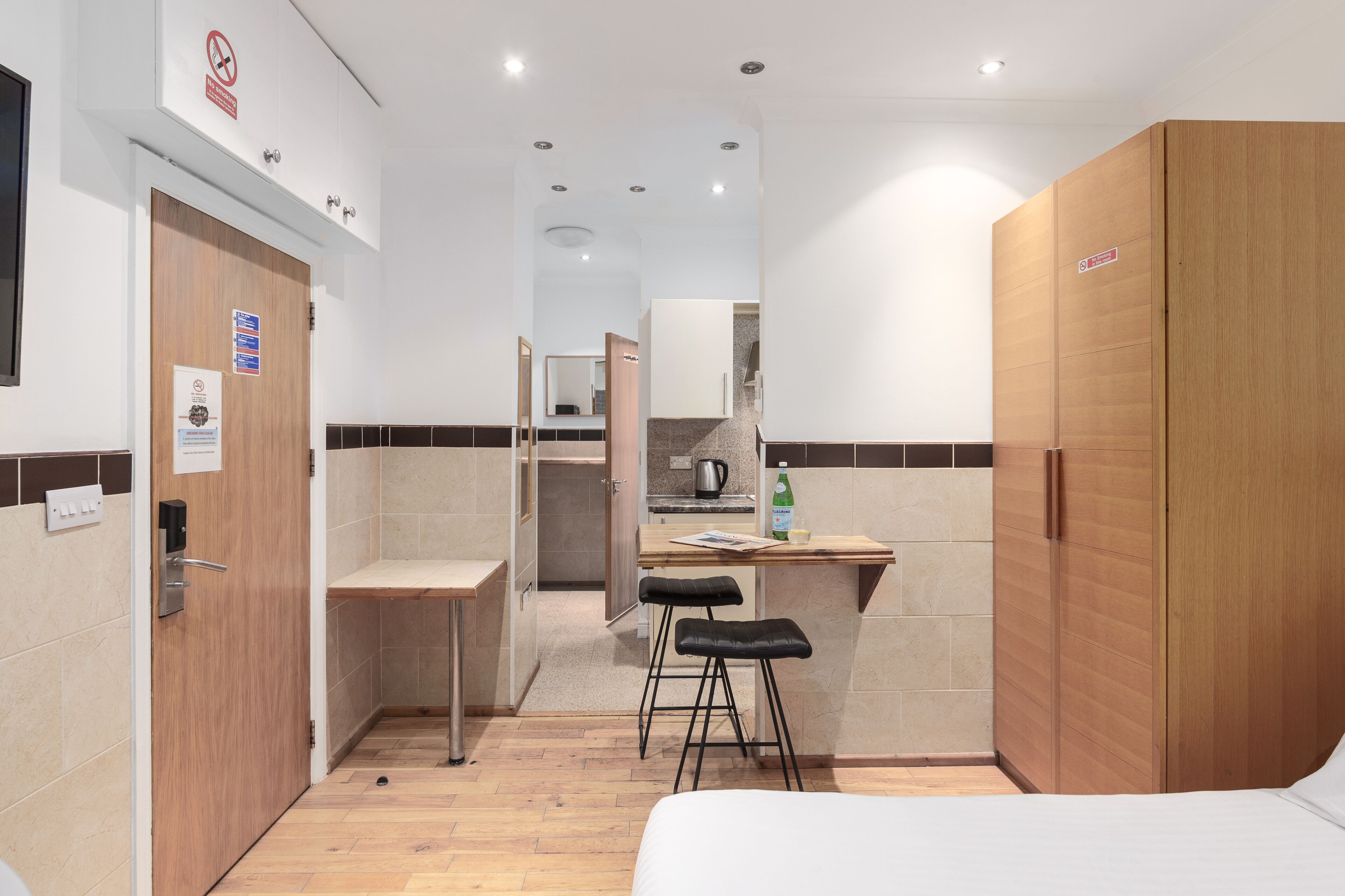 Une chambre d’hôtel de taille réduite, comprenant un lit, une armoire en bois, une petite kitchenette et une salle de bain.