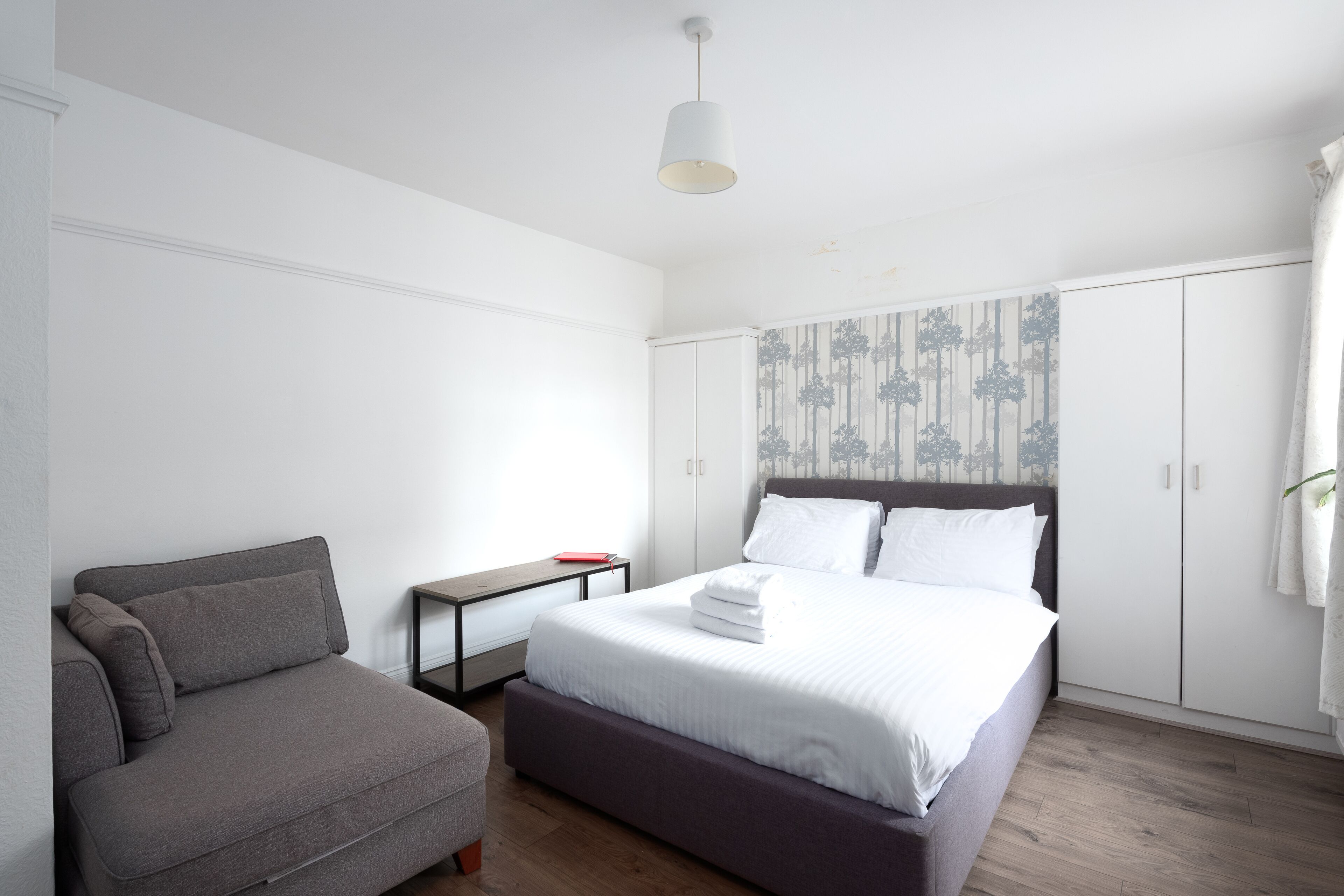 Quarto com cama, sofá, guarda-roupa e mesa de cabeceira.