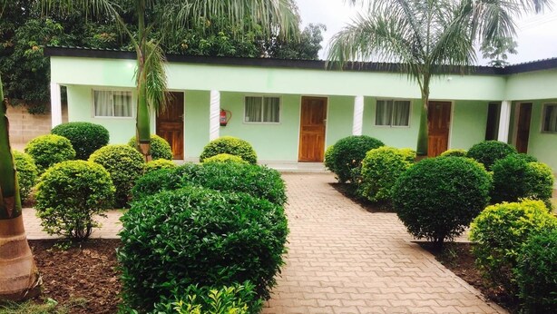 A courtyard with a paved walkway, neatly trimmed bushes, and a building with a green facade and wooden doors. - Richland Lodge Motel (Livingstone)