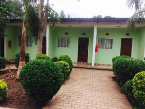 A green building with a paved entrance, surrounded by well-maintained bushes and a palm tree. - Richland Lodge Motel (Livingstone)