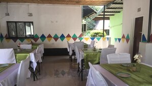 A dining area with tables set for four, each covered with a white tablecloth and a green table runner. The room has a tiled floor and a window with a view of greenery outside. - Richland Lodge Motel (Livingstone)