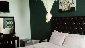 A neatly made bed with a floral bedspread, a dark tufted headboard, a bedside table, a lamp, and a wall-mounted TV. - Richland Lodge Motel (Livingstone)