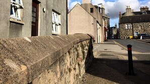 A street with buildings, a stone wall, and a bollard. - Morris Gardens Apartments (Inverurie)
