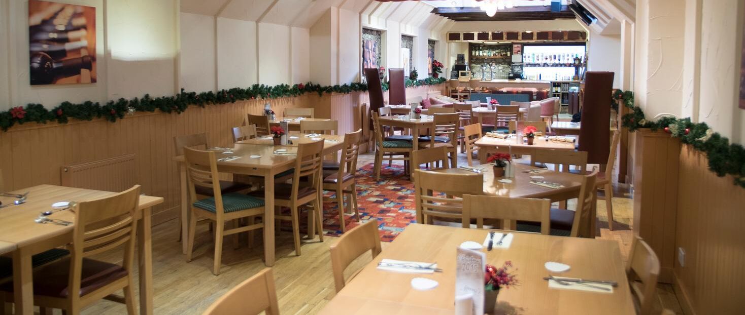 En restaurant med træborde og stole, en julekrans og et barområde i baggrunden.