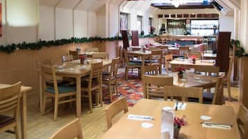 A restaurant with wooden tables and chairs, a Christmas garland, and a bar area in the background.