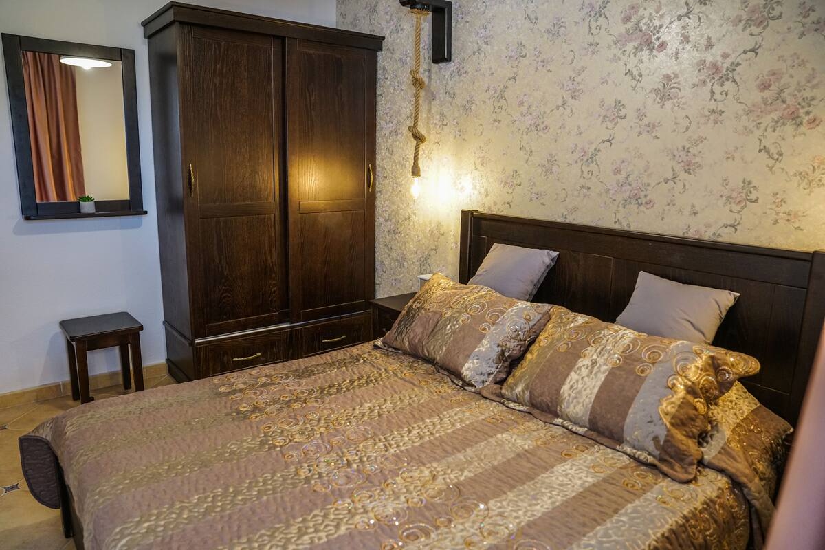 Ein Schlafzimmer mit einem großen Bett, einem Kleiderschrank, einem kleinen Tisch und einem Spiegel.