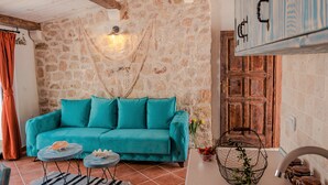 A cozy living room with a teal sofa, a stone wall, a wooden door, and a hanging light fixture. - Apartments Bazar (Ulcinj)