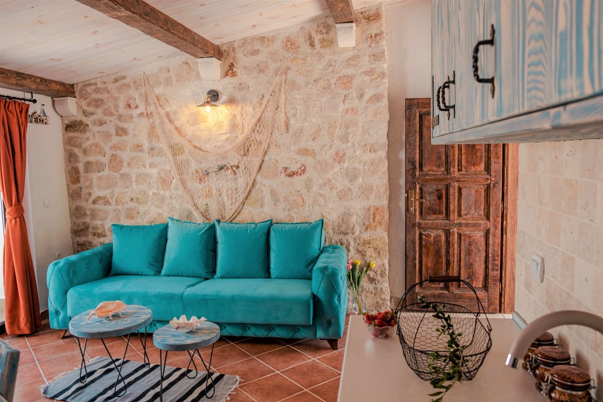 Ein gemütliches Wohnzimmer mit einem türkisfarbenen Sofa, einer Steinwand, einer Holztür und einer Pendelleuchte.