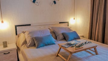 A neatly made bed with a wooden headboard, two bedside tables, and a small wooden table with a magazine and decorative items.