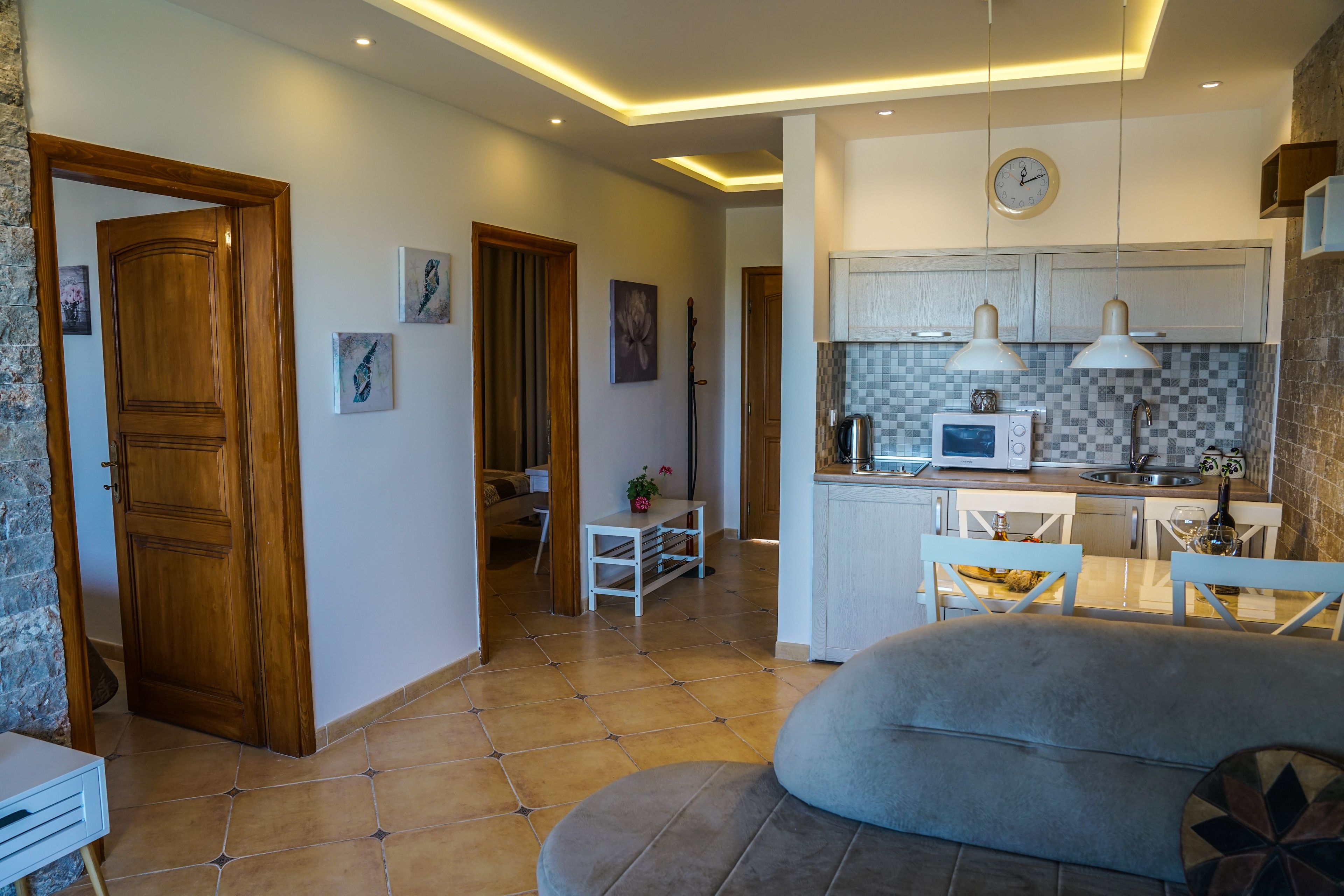 A modern kitchen with white cabinets, a microwave, and pendant lights. There is a dining area with a table and chairs, and a living room with a sofa.
