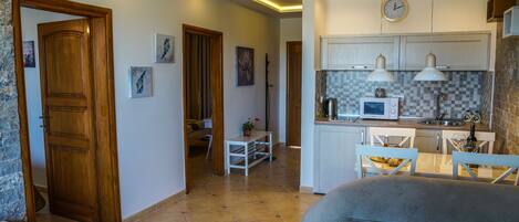A modern kitchen with white cabinets, a microwave, and pendant lights. There is a dining area with a table and chairs, and a living room with a sofa.