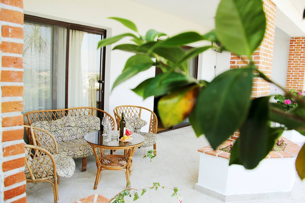 Eine Terrasse mit Korbmöbeln, einem Glastisch und einem weißen Blumentopf mit Blumen.