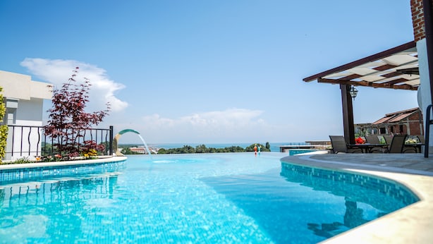 A swimming pool with clear blue water, surrounded by a patio area with chairs and a pergola. - Apartments Bazar (Ulcinj)