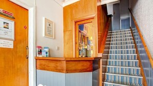 A reception area with a wooden counter, a sign reading "OYO", and a staircase with striped carpet. - Godolphin Arms Hotel (Newquay)