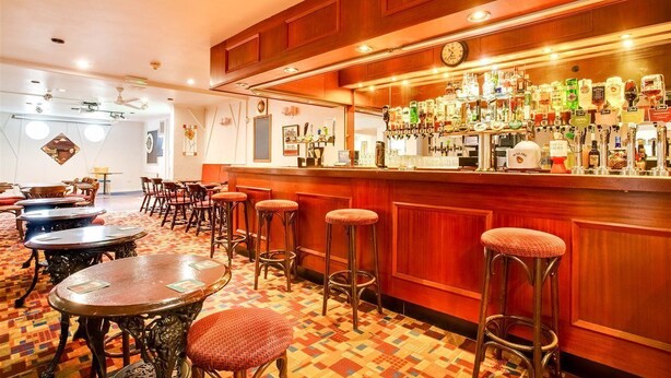 A bar area with wooden paneling, a variety of liquor bottles, and several stools. - Godolphin Arms Hotel (Newquay)