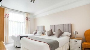 A hotel room with a large bed, two bedside tables, a chair, and a window with curtains. - Godolphin Arms Hotel (Newquay)