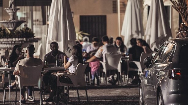 Un café al aire libre con mesas, sillas, una fuente y sombrillas.