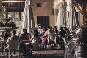 Un café en plein air avec des tables, des chaises, une fontaine et des parasols.